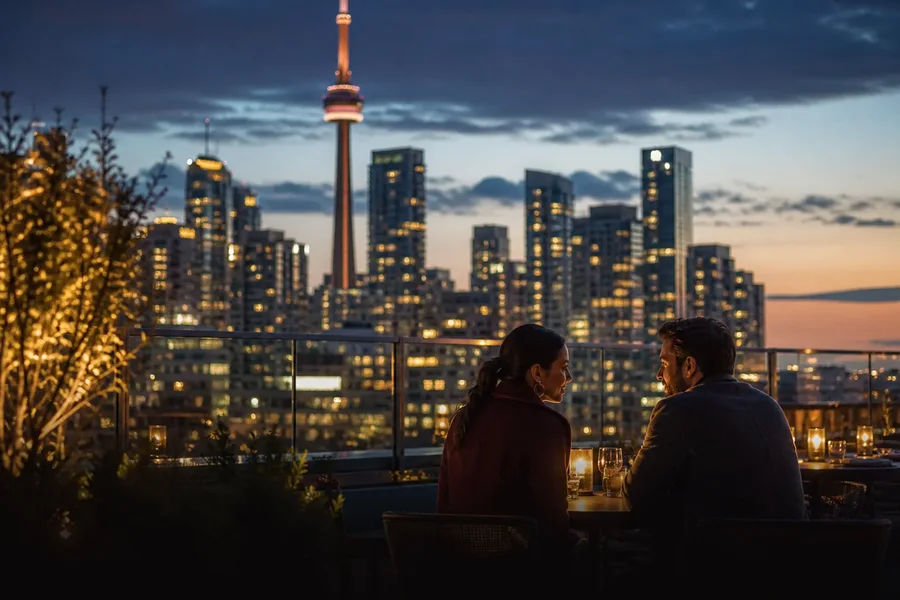 A couple dining on a Toronto rooftop with the CN Tower skyline at dusk